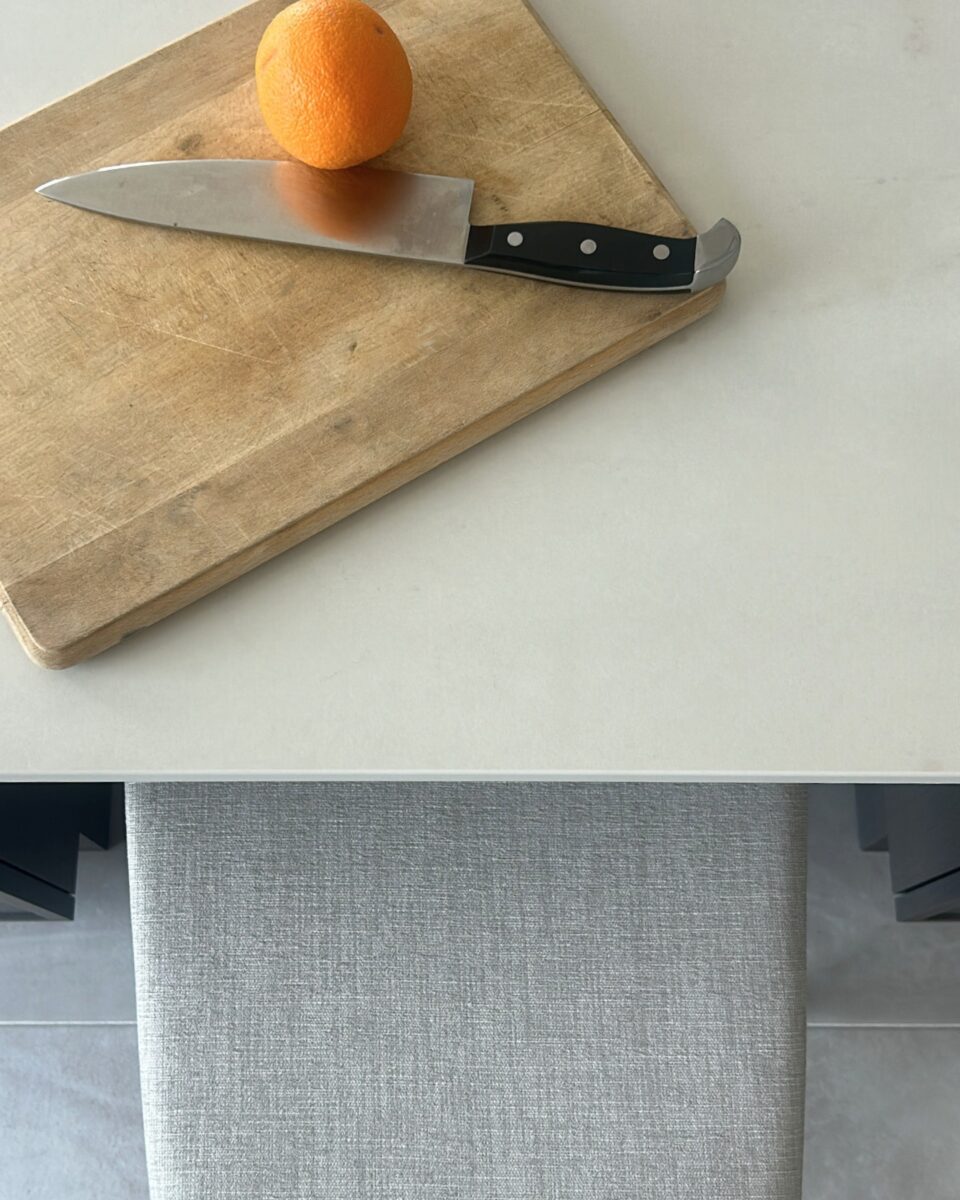 Comptoir découper pour cusinier. Banc en tissu pale et comptoir marbre mat. Ceramic gris pale et armoires de cuisine miralis brun foncé avec poignées noirs.