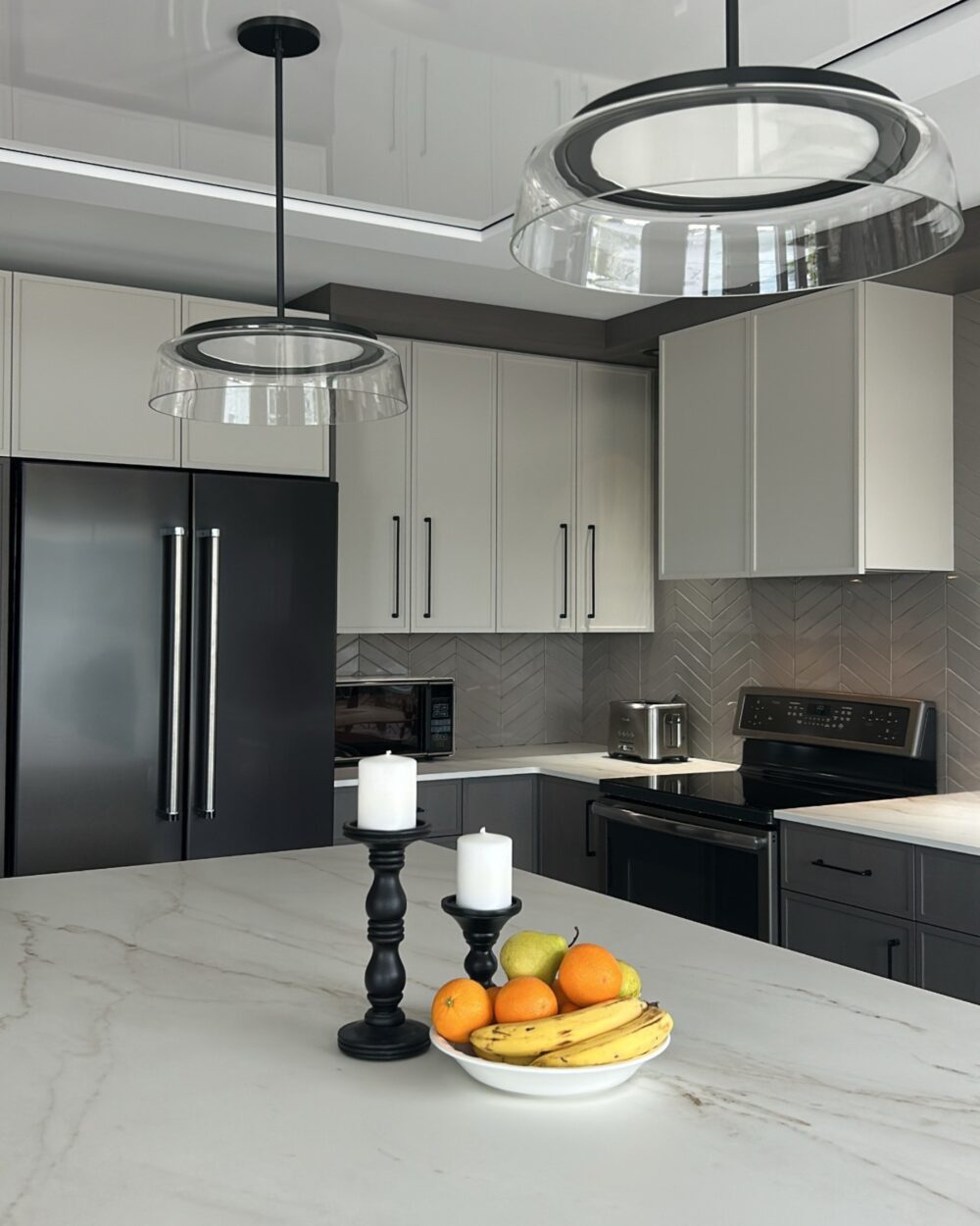 Cuisine moderne Miralis avec comptoir en mabre mat. Luminaires suspenduset armoires blanches avec poignées argentées.