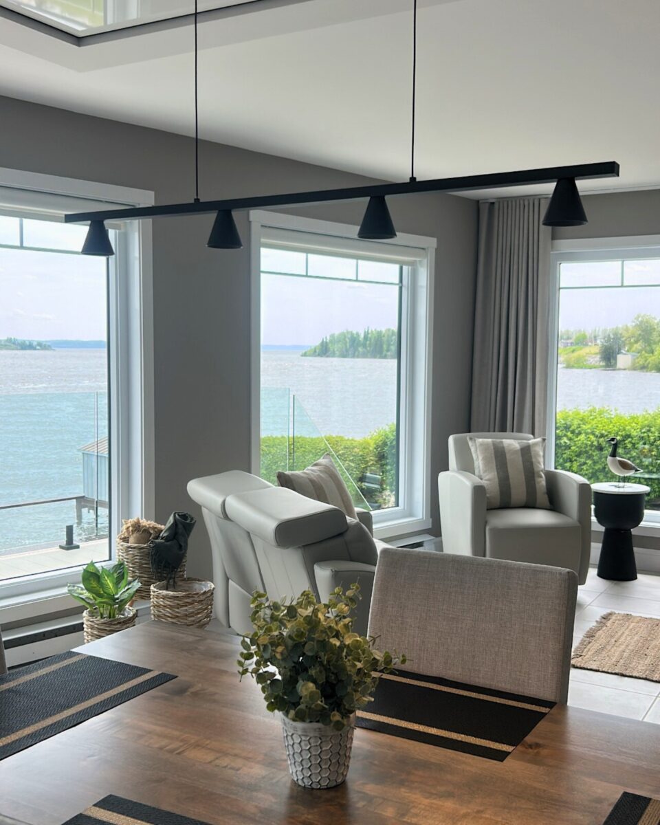 Salle à manger, adjacente au salon, avec vue sur le lac. Pieces lumineuses et modernes, decorer au gout du jour. Divan en cuir. Luminaire suspendu noir et table à manger en bois brun foncé.